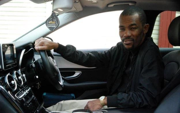 Serge Cabonge seated in a car, wearing a black shirt and looking toward the camera.